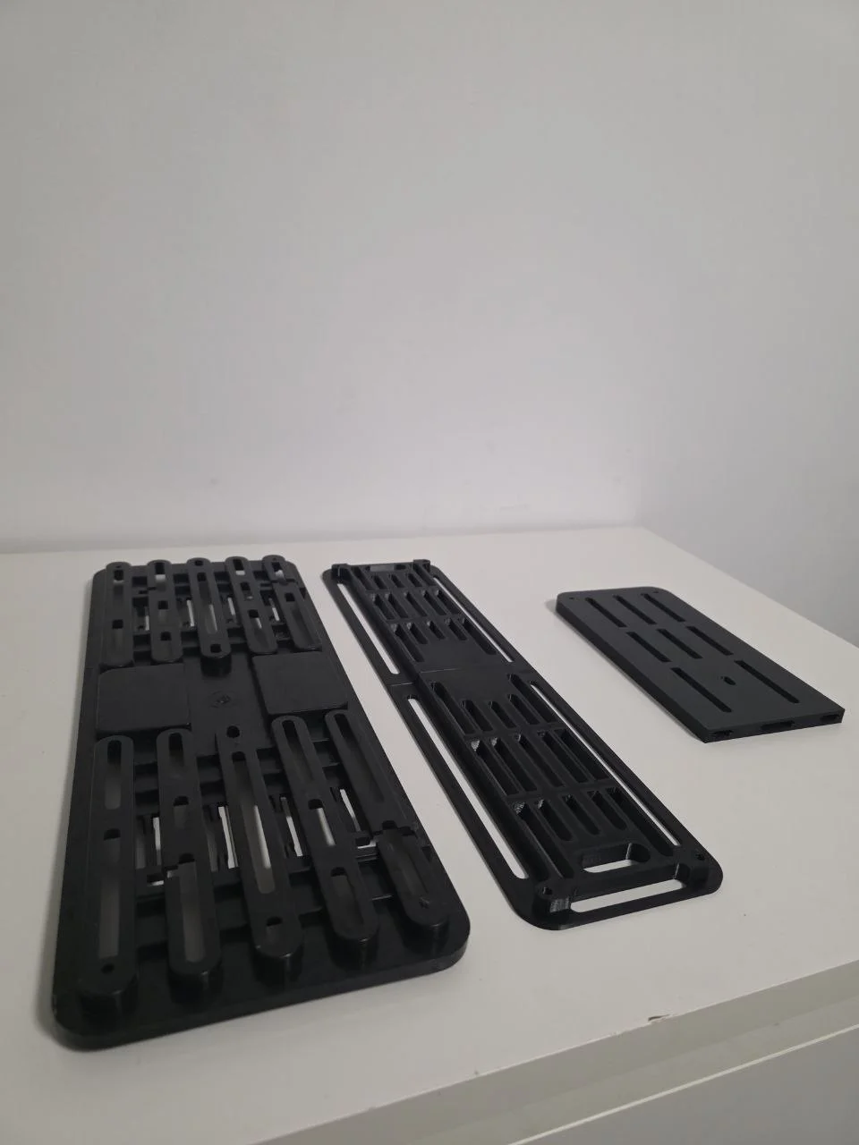 Three rear plate holders — left: original factory holder · centre: Stage 1 final (largest) · right: first prototype half